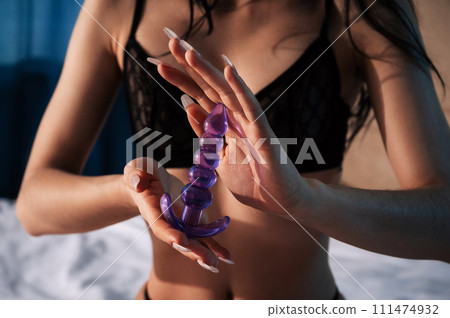 silicone butt anal plug in the hands of a woman girl with a sexy body in underwear sitting on bed in bedroom. Female sex toys for anal sex and orgasm 111474932
