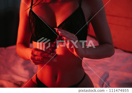 silicone butt anal plug in hands of a woman with a sexy body and breasts in bra sitting on bed in bedroom. Female sex toys for anal sex and orgasm 111474935