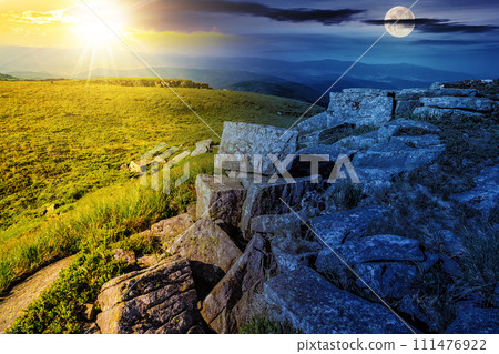 landscape with stones on the hillside with sun and moon at twilight. day and night time change on summer solstice concept. mysterious mountain scenery with green alpine meadows in morning light landscape with stones on the hillside with sun and moon at twilight. day and night time change on summer solstice concept. mysterious mountain scenery with green alpine meadows in morning light 111476922