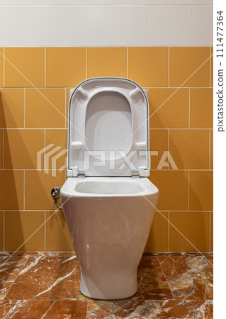 Modern toilet with open lid and seat against a contrasting yellow and white tiled wall Modern toilet with open lid and seat against a contrasting yellow and white tiled wall 111477364