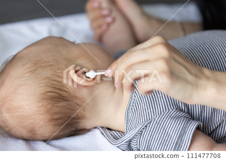 Female hand with cotton swab near ear of a baby. Closeup. 111477708