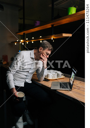 Vertical shot of thoughtful businessman working late at night in office workplace, focused on digital marketing project. Male manager working with computer and cup of coffee, trying to meet deadline. 111478264