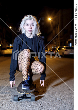 Front view of young woman in shorts on a long board while looking camera at night in the city 111478627
