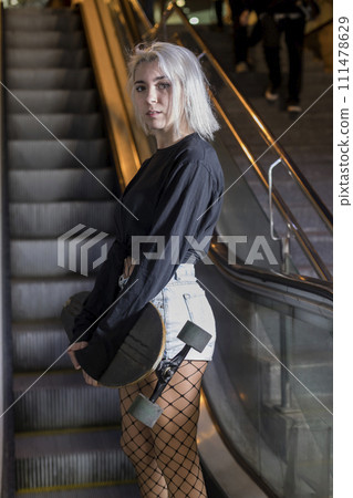 woman looking camera in shorts holding a long board while standing on mechanic stairs at night 111478629