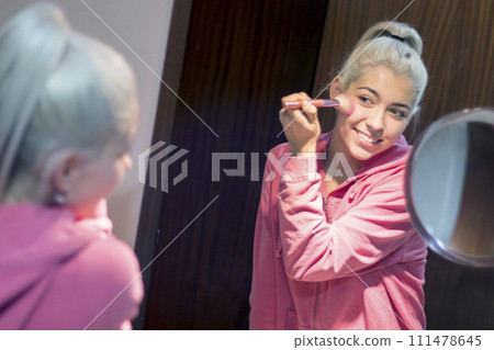 Blonde beautiful woman doing makeup in front of mirror Blonde beautiful woman doing makeup in front of mirror 111478645