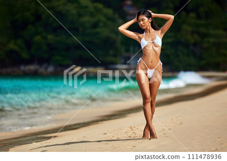 Beautiful asian girl in white bikini posing at the tropical beach Beautiful asian girl in white bikini posing at the tropical beach 111478936