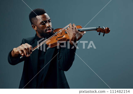 African American man in black suit playing violin, creating soulful music on gray background African American man in black suit playing violin, creating soulful music on gray background 111482154