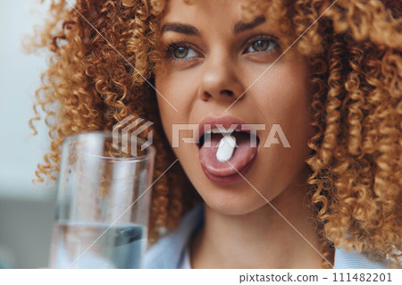 Woman with curly hair swallowing pill with glass of water in hand, healthcare and medication concept Woman with curly hair swallowing pill with glass of water in hand, healthcare and medication concept 111482201
