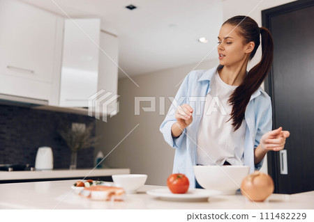 A woman preparing healthy salad in the kitchen with fresh vegetables and a bowl of mixed greens A woman preparing healthy salad in the kitchen with fresh vegetables and a bowl of mixed greens 111482229