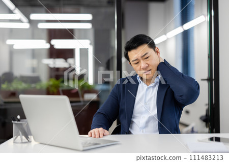 Overworked overtired asian man in business suit at workplace inside office, businessman has severe pain in neck, massaging muscle , long time sitting work with laptop, daily business of financier. Overworked overtired asian man in business suit at workplace inside office, businessman has severe pain in neck, massaging muscle , long time sitting work with laptop, daily business of financier. 111483213