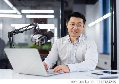 Portrait business coach, male mentor recording audio podcast in studio, businessman working with laptop, using professional microphone, teacher smiling, looking at camera, financier training course. 111483219