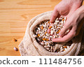 Hands scooping diverse colorful heirloom beans from a rustic eco bag. Whole foods and healthy eating in sustainable packaging 111484756