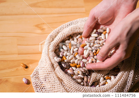 Hands scooping diverse colorful heirloom beans from a rustic eco bag. Whole foods and healthy eating in sustainable packaging 111484756
