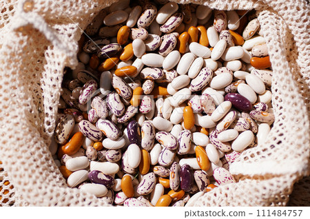 Close-up shot of heirloom beans spilling from a mesh eco bag on wood surface. Organic produce or vegetarian ingredients 111484757