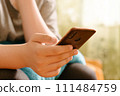 Close-up of hands holding a smartphone, Person texting message on Smartphone, with blurred background in warm natural light. Mobile technology in everyday life. Social media interaction 111484759