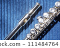 Close-up of silver flute with detailed view of mouthpiece, shiny surface and keys of instrument on blue fabric background, emphasizes the flute's elegance. Instrument maintenance and care 111484764