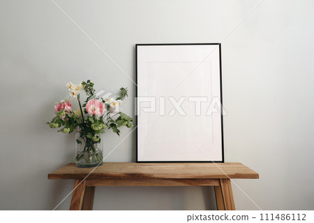 Easter springtime still life. Blank black picture frame mockup on wooden bench, table. Spring bouquet of pink tulips, white daffodils, hawthorn flowers. Pastel green, mint wall background. Easter springtime still life. Blank black picture frame mockup on wooden bench, table. Spring bouquet of pink tulips, white daffodils, hawthorn flowers. Pastel green, mint wall background. 111486112