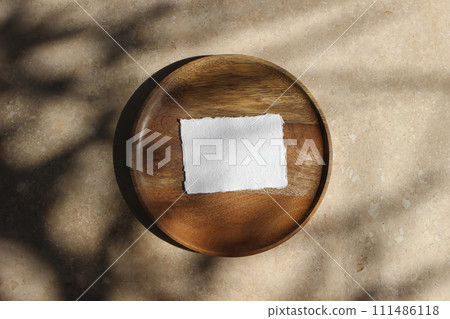 Boho wedding invitation. Blank greeting, business card mockup on wooden tray in sunlight. Harsh tree branches shadows. Beige marble stone texture, background. Summer stationery template. Flat lay, top 111486118