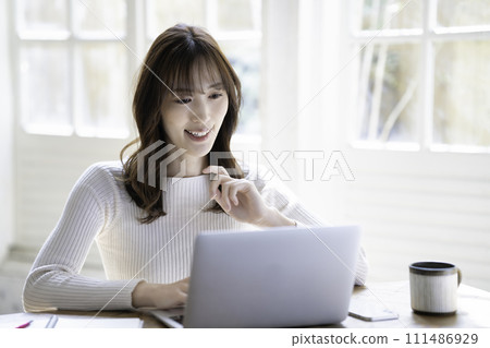 A woman using a laptop in a bright room with sunlight shining through it 111486929