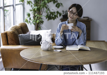Middle-aged woman reading while drinking tea in the living room Middle-aged woman reading while drinking tea in the living room 111487193