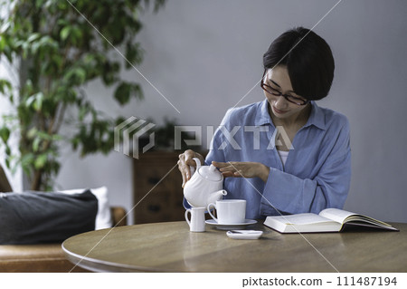 Middle-aged woman reading while drinking tea in the living room Middle-aged woman reading while drinking tea in the living room 111487194