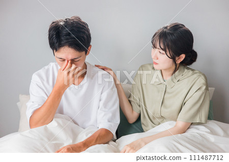 A man suffering from eye strain, dry eyes, cataracts, and glaucoma and a worried woman/couple in the morning in the bedroom 111487712
