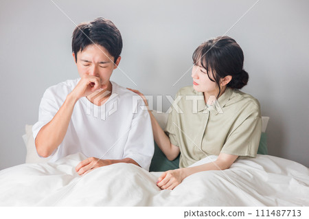 A man suffering from hay fever, rhinitis, and a runny nose and a worried woman/couple in the morning in the bedroom 111487713