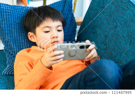 Elementary school boy lying on the sofa and using a smartphone 111487995