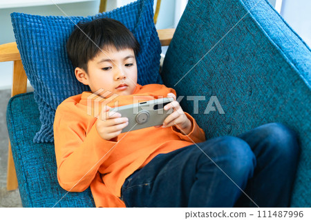 Elementary school boy lying on the sofa and using a smartphone Elementary school boy lying on the sofa and using a smartphone 111487996