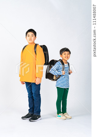 Elementary school siblings lined up with school bags on their backs 111488007