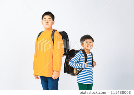 Elementary school siblings lined up with school bags on their backs 111488008