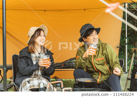 Male and female campers making camping food and drinking beer at a campsite in autumn and winter 111488224