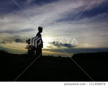 The man standing in the middle of the evening twilight in traditional clothes was in a wide area and looked like a shadow The man standing in the middle of the evening twilight in traditional clothes was in a wide area and looked like a shadow 111490678