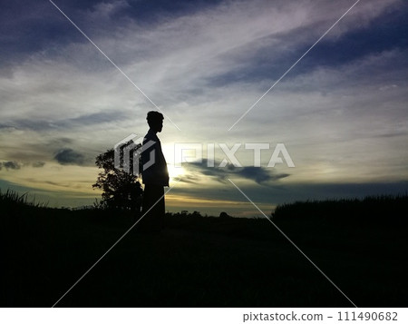 The man standing in the middle of the evening twilight in traditional clothes was in a wide area and looked like a shadow The man standing in the middle of the evening twilight in traditional clothes was in a wide area and looked like a shadow 111490682