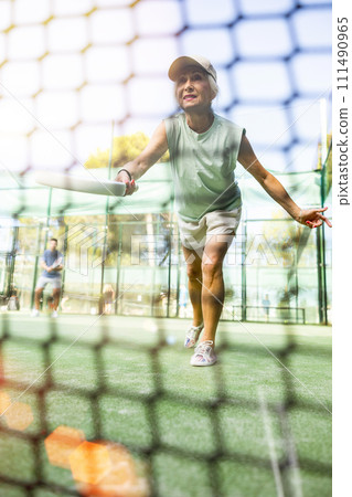 View through tennis net of elderly woman playing paddle tennis outdoor 111490965