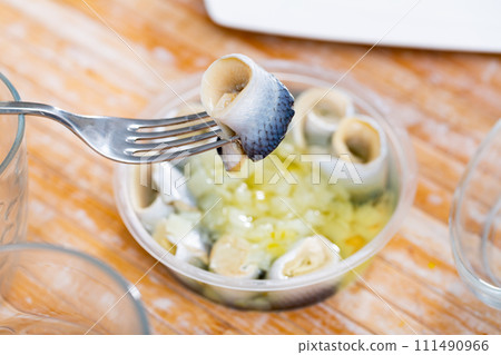 Invisible hand holds fork with pierced piece of salted herring fillet 111490966