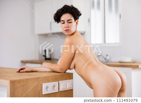 Sexual, emotional nude woman standing and leaning on wooden table in cuisine at home 111491079
