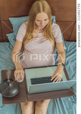 Multitasking expectant woman enhances her home workspace, using an aroma diffuser for a soothing atmosphere while working during pregnancy 111491759