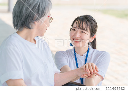 Elderly people in wheelchairs and caregivers (helpers/physiotherapists) talking while walking in hospitals/nursing facilities 111493682
