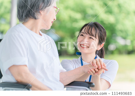 Elderly people in wheelchairs and caregivers (helpers/physiotherapists) talking while walking in hospitals/nursing facilities 111493683