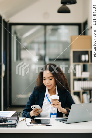Confident beautiful businesswoman typing laptop and digital tablet while holding coffee . Confident beautiful businesswoman typing laptop and digital tablet while holding coffee . 111494134