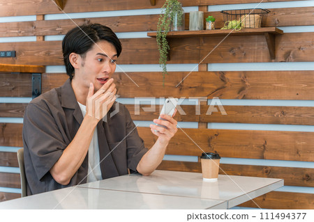 A young Asian man using a smartphone at a cafe, home, etc. (surprise, surprise, surprise, discovery) A young Asian man using a smartphone at a cafe, home, etc. (surprise, surprise, surprise, discovery) 111494377