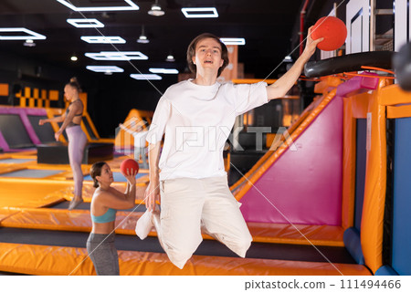 Active European young male in sportswear playing basketball while bouncing on colorful trampolines indoors in leisure sports center 111494466