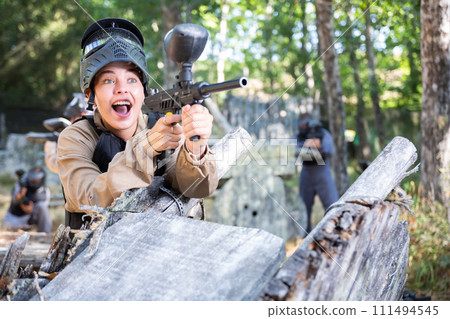 Excited girl paintball player aiming with paintball gun and shooting 111494545