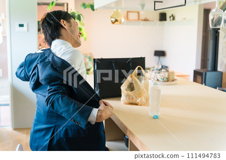 An Asian businessman in a suit takes off his jacket and jacket at the dining room after returning home. 111494783