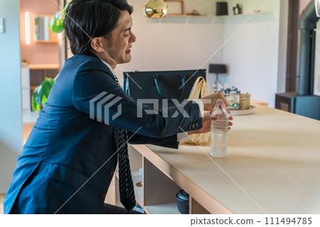 An Asian businessman in a suit opens a plastic bottle in the dining room after returning home 111494785