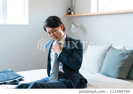 一位穿著疲憊西裝的年輕商人坐在床上（疲勞、辦公室工作、加班、早上回家、辛苦工作） 111494794