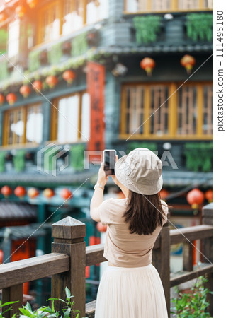 woman traveler visiting in Taiwan, Tourist taking photo and sightseeing in Jiufen Old Street village with Tea House background. landmark and popular attractions near Taipei city. Travel concept 111495180