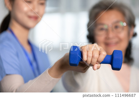 Asian female doctor advice elderly patient to physiotherapist to exercise with dumbbell at home.Smiling nurse helping senior patient workout exercise to build muscle strong.Physiotherapist Nursing. 111496687