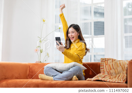 Millennial asian young woman looking mobile phone laughing with good news or discount voucher for shopping online at home.Happy and cheerful woman looking on cellphone app read message feel excited Millennial asian young woman looking mobile phone laughing with good news or discount voucher for shopping online at home.Happy and cheerful woman looking on cellphone app read message feel excited 111497002
